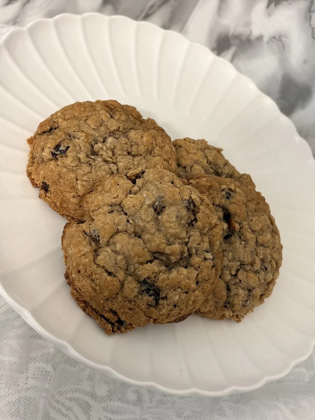 Three large soft-baked oatmeal cookies stacked on a scalloped white plate